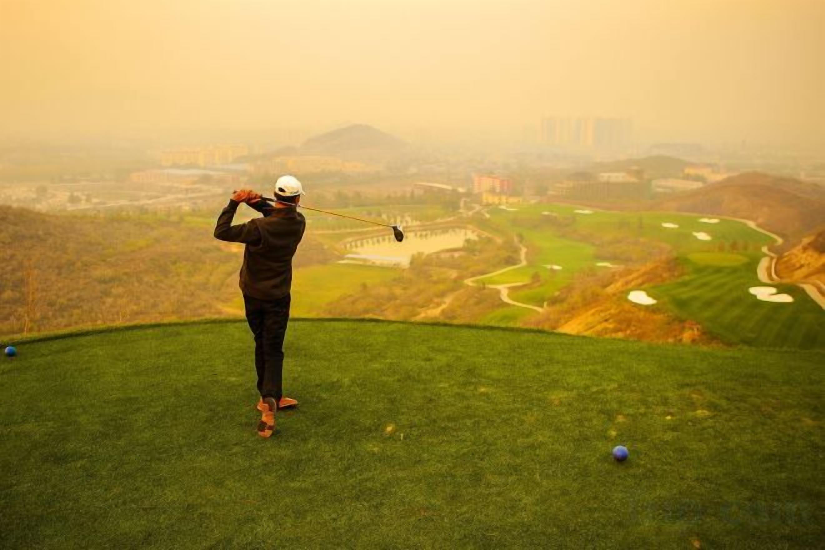 Uma pessoa joga golfe num campo com vista para edifícios ao longe.