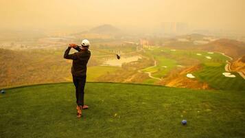 Uma pessoa joga golfe num campo com vista para edifícios ao longe.