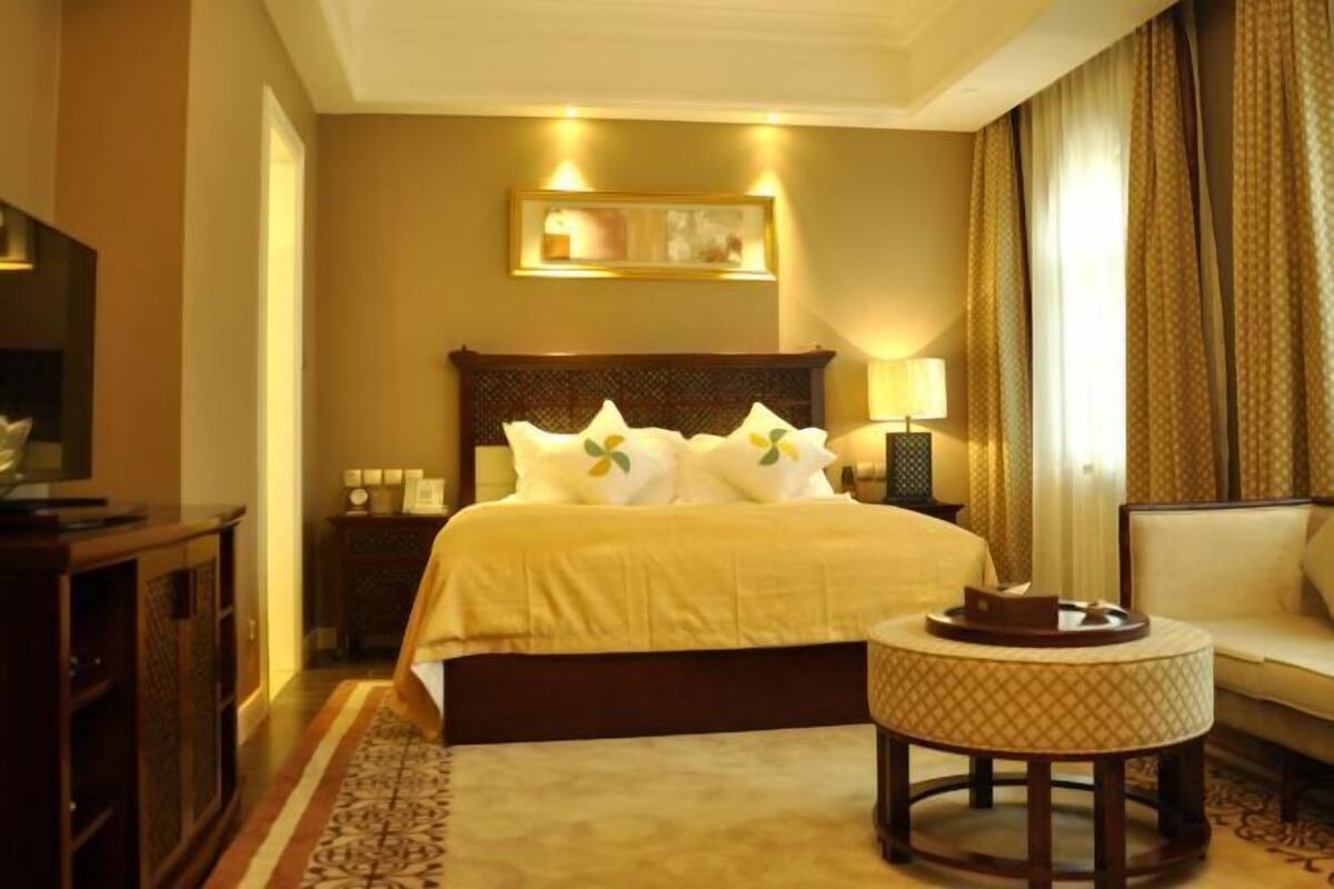A hotel room with a large bed, a round side table, a sofa, a TV, and a framed picture on the wall.