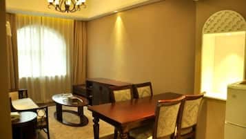 Habitación de hotel con comedor que incluye una mesa y sillas de madera, una mesa redonda pequeña, una araña y una ventana con cortinas.