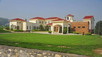 A large, multi-story building with a symmetrical facade, a central courtyard, and a stone wall in the foreground.