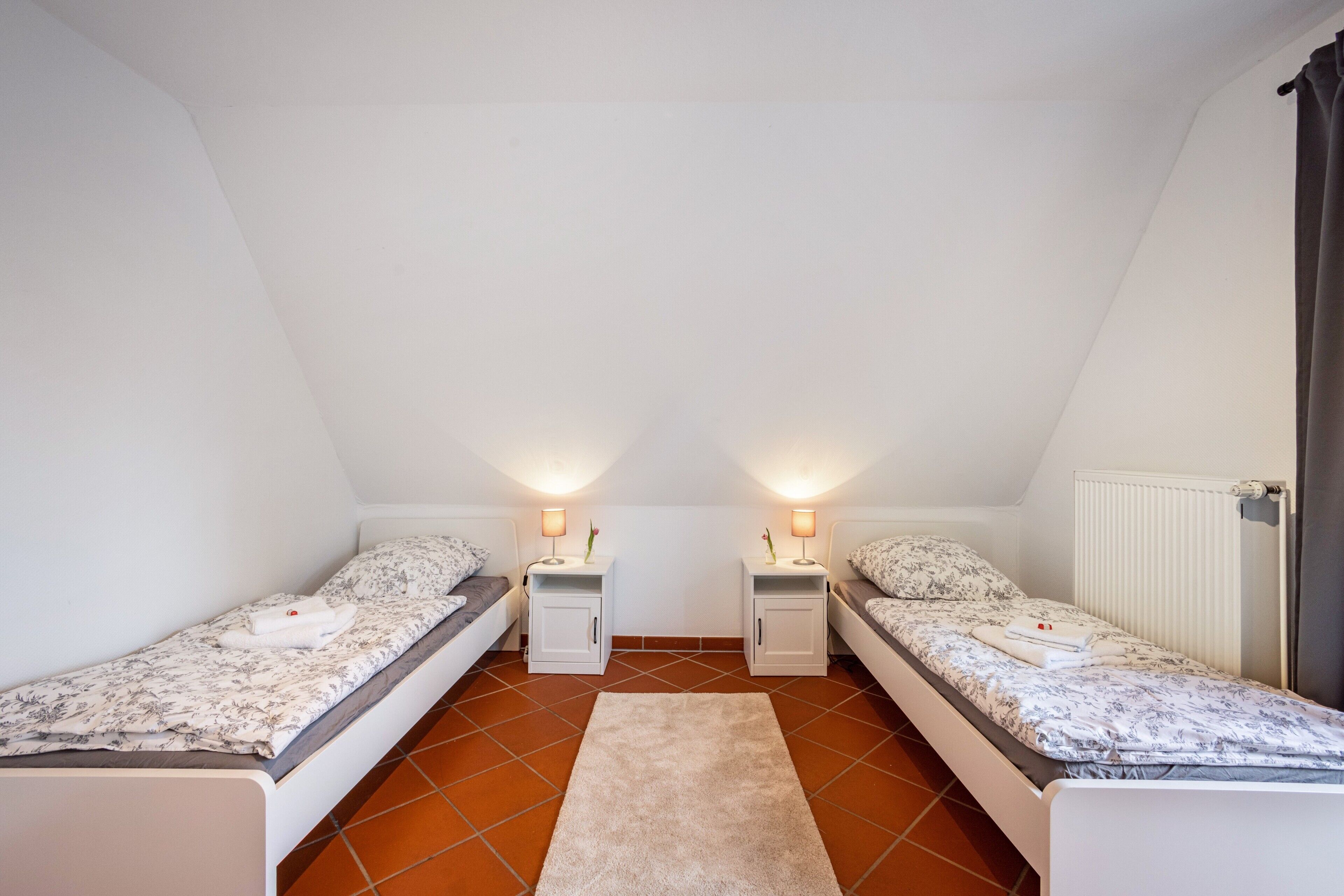 A small, triangular attic bedroom with two single beds, nightstands, and a radiator.
