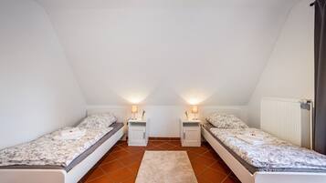 A small, triangular attic bedroom with two single beds, nightstands, and a radiator.