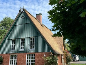 Een traditioneel huis met rieten dak, een steil dak, een schoorsteen en een fundering van baksteen.