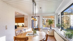 A dining area with a wooden table and chairs, a pendant light, and a view of the outdoors through a large window. - Haus Sonneck - Apartment 5 with Mountain View, Private Terrace, and Wi-Fi (Willingen (Upland))