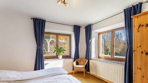 A bedroom with two beds, a chair, a radiator, and large windows with curtains. - Haus Sonneck - Apartment 5 with Mountain View, Private Terrace, and Wi-Fi (Willingen (Upland))