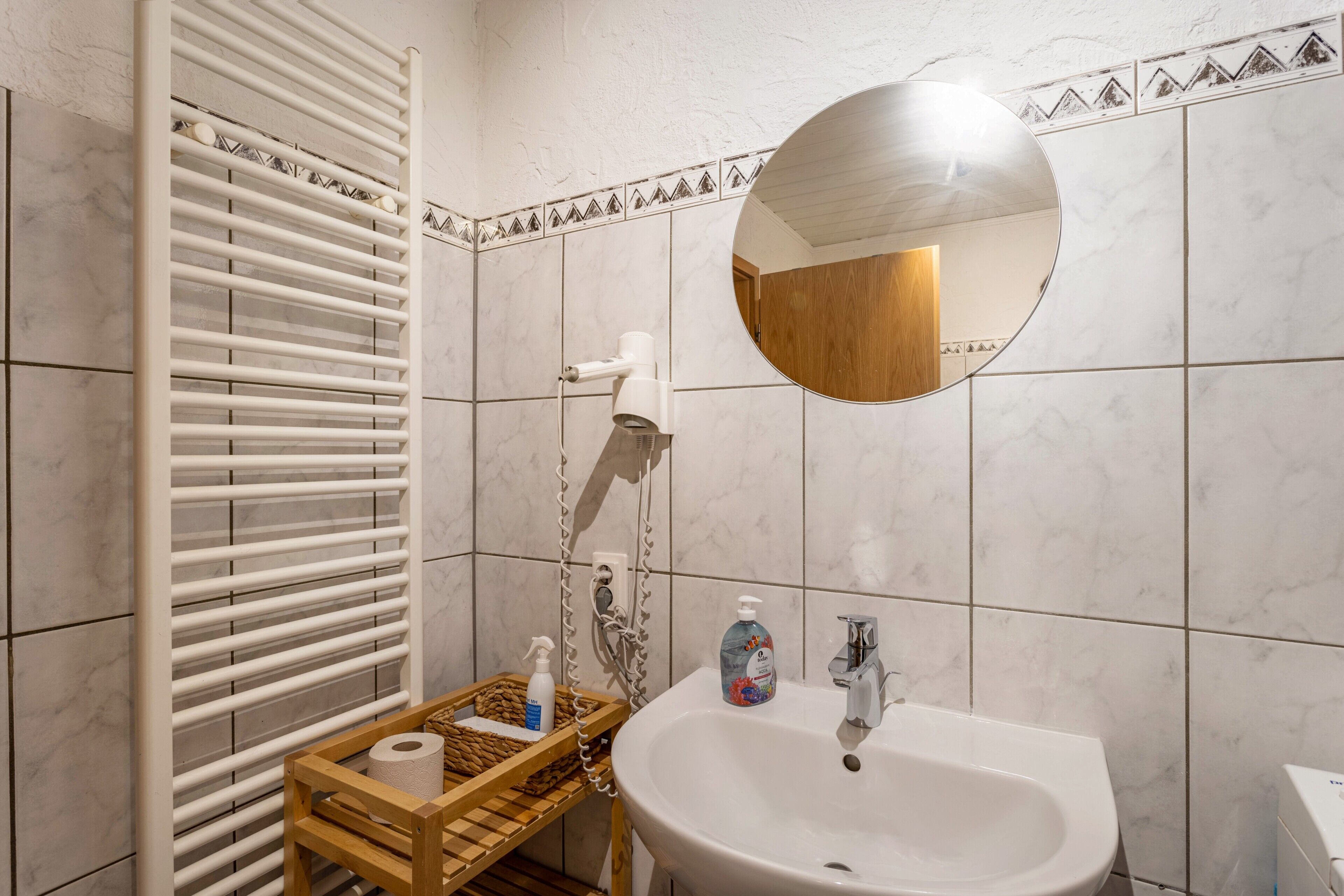A bathroom with a white sink, a mirror, a towel rack, and a shower area.