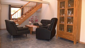 A living room with a staircase, two armchairs, a small table with a vase, and a wooden cabinet with glass doors. - Holiday Apartment 'Ferienhaus Op'n Doerp' with Private Terrace, Garden, Wi-Fi & EV Charger (Oesterwurth)
