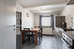 Una cocina compacta con una mesa, sillas, refrigerador, estufa y ventana con cortinas.