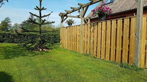 A wooden fence, a well-maintained lawn, and a coniferous tree. - Holiday Apartment 'Ferienhaus Op'n Doerp' with Private Terrace, Garden, Wi-Fi & EV Charger (Oesterwurth)