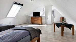 A bedroom with a bed, a dresser, a table with a vase, a TV on a stand, and a skylight. - Holiday Apartment 'Ferienhaus Op'n Doerp' with Private Terrace, Garden, Wi-Fi & EV Charger (Oesterwurth)