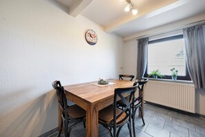 Un comedor con una mesa de madera, cuatro sillas, un reloj en la pared y una ventana con cortinas.