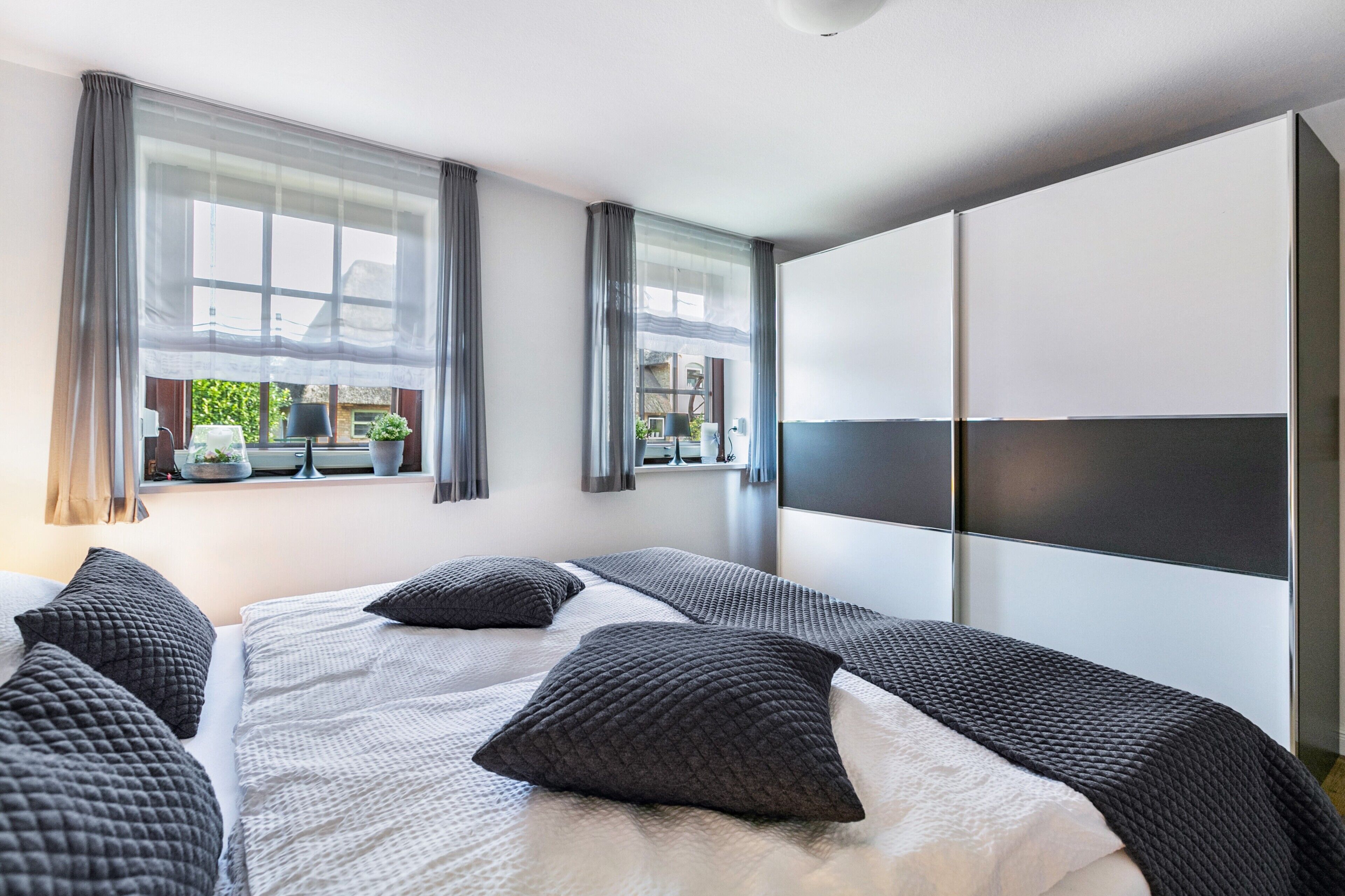 Ein modernes Hotelzimmer mit einem großen Bett, zwei Nachttischen, einem Kleiderschrank und einem Vorhangfenster.