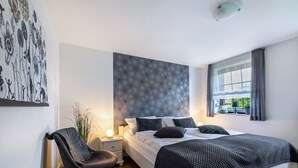 Ein modernes Schlafzimmer mit Bett, Nachttisch, Sessel und einer Wand mit Blumenmuster.