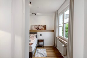Ein Schlafzimmer mit einem Bett, einem Nachttisch, einer Lampe, einem Heizkörper und einem Fenster mit Vorhängen.