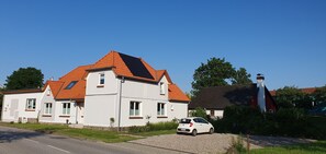 Ein zweistöckiges Haus mit rotem Ziegeldach, weißer Fassade und einem parkenden Auto davor.