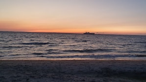 Una playa con olas, un barco a lo lejos y un cielo despejado.