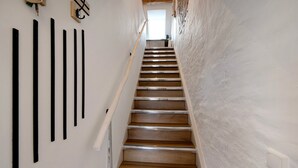 Una escalera con peldaños de madera y barandillas metálicas que conduce a una habitación con paredes blancas y una ventana.