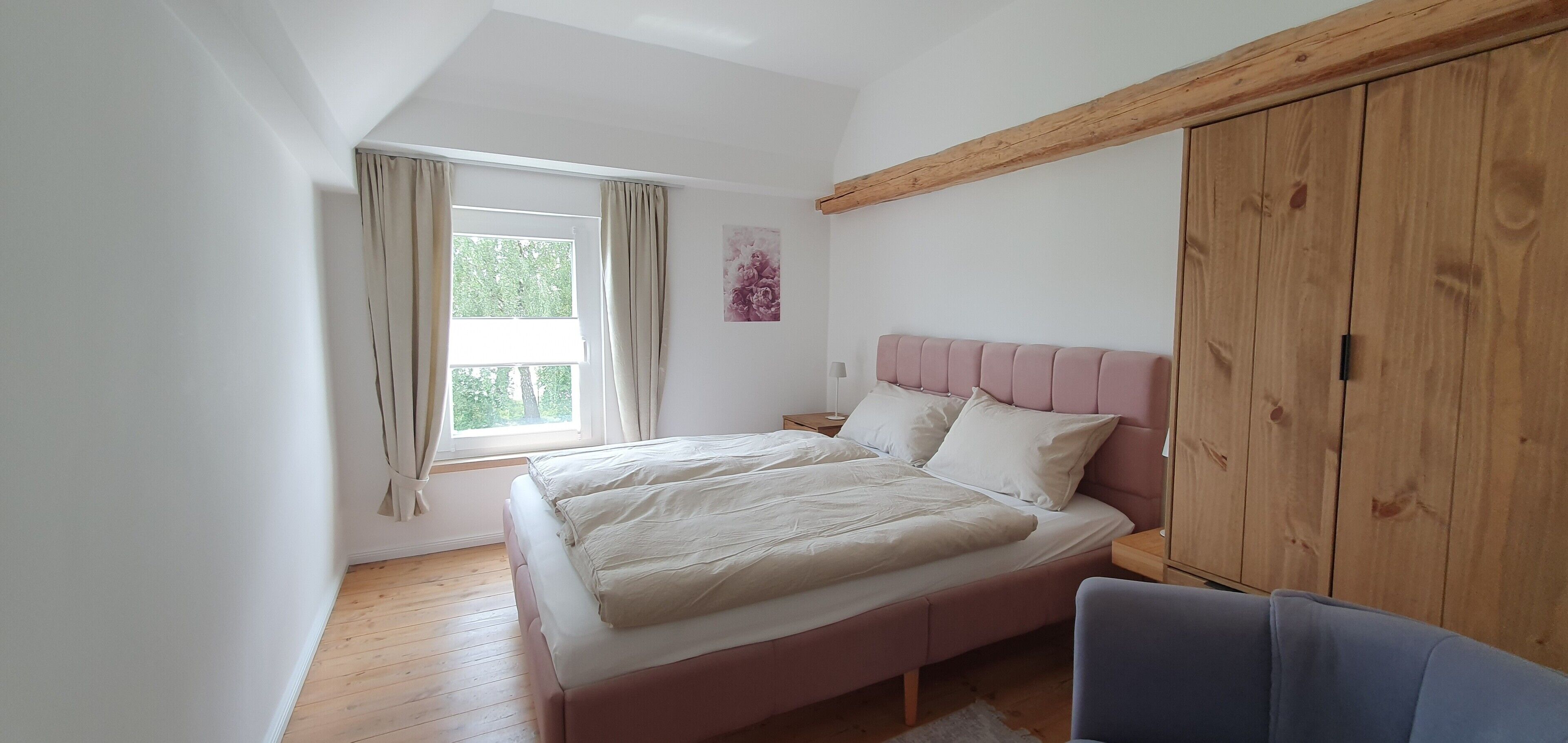 Une chambre à coucher avec un lit, une fenêtre avec des rideaux, une armoire en bois et une table de chevet avec une lampe.