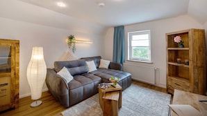 Una sala de estar moderna con un sofá modular, una lámpara de pie, un mueble de madera y un ventanal con cortinas.