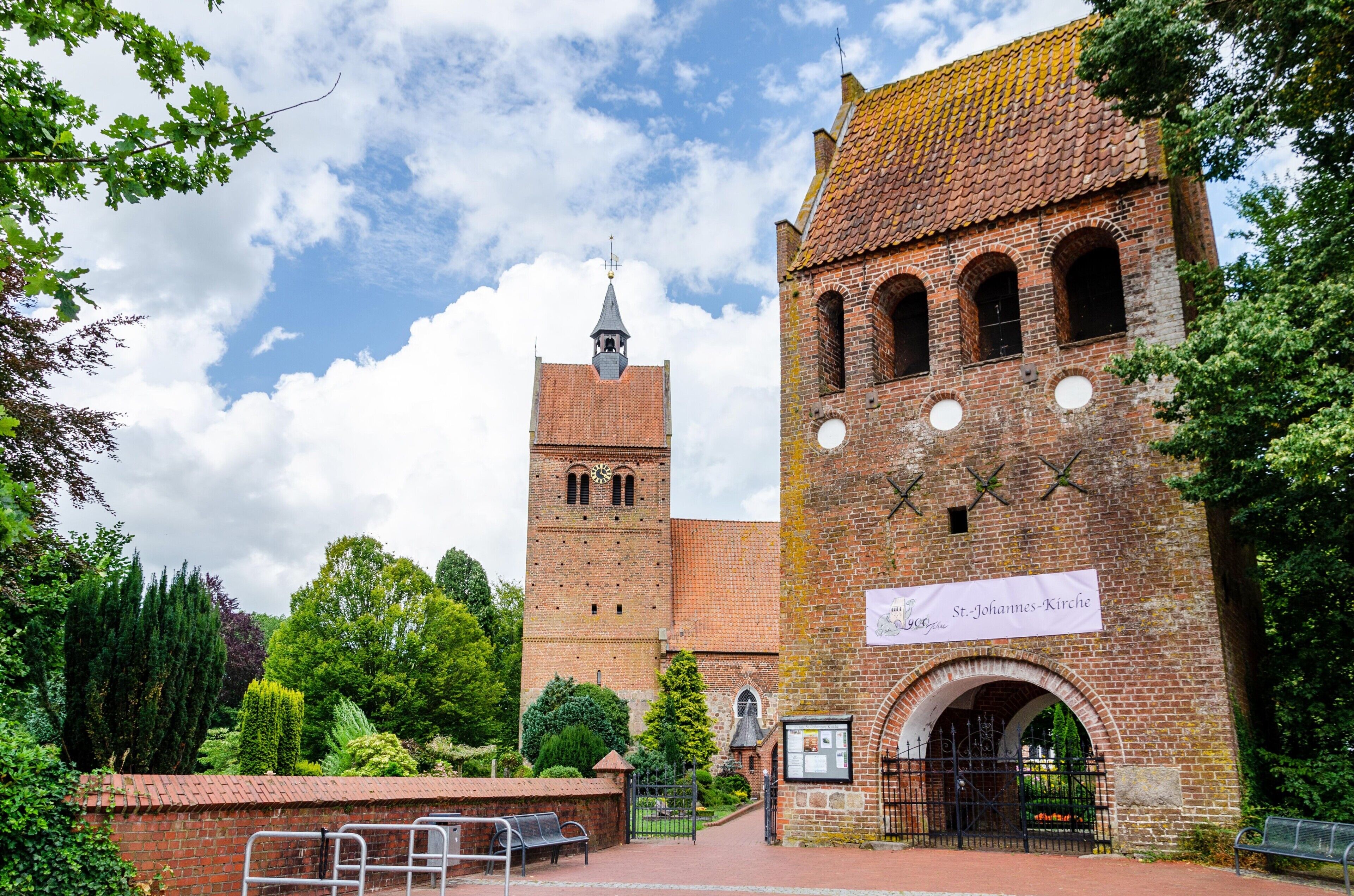 Une église historique, dotée d’un clocher imposant et d’une entrée en arc de cercle, entourée d’une végétation luxuriante.