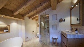 A modern bathroom with a freestanding bathtub, a glass-enclosed shower, and a wooden vanity with a mirror. - Apartment 'Steinbock B' with Mountain View, Balcony and Wi-Fi (Klosters-Serneus)