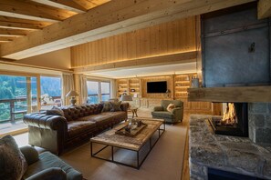 Ein geräumiges Wohnzimmer mit einer Ledersofa, einem Kamin aus Stein und einem an einer Holzvertäfelung befestigten Fernseher.