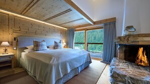 A bedroom with a bed, nightstands, a fireplace, and a large window with curtains. - Apartment 'Steinbock B' with Mountain View, Balcony and Wi-Fi (Klosters-Serneus)