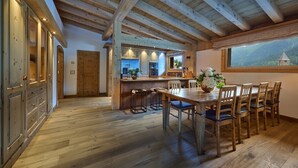 A spacious kitchen with wooden beams, a dining area with a wooden table and chairs, and a view of a mountain through a window. - Apartment 'Steinbock B' with Mountain View, Balcony and Wi-Fi (Klosters-Serneus)