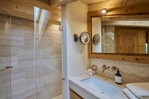 A bathroom with a wooden ceiling, a glass shower door, a sink with a mirror, and a towel on the counter.