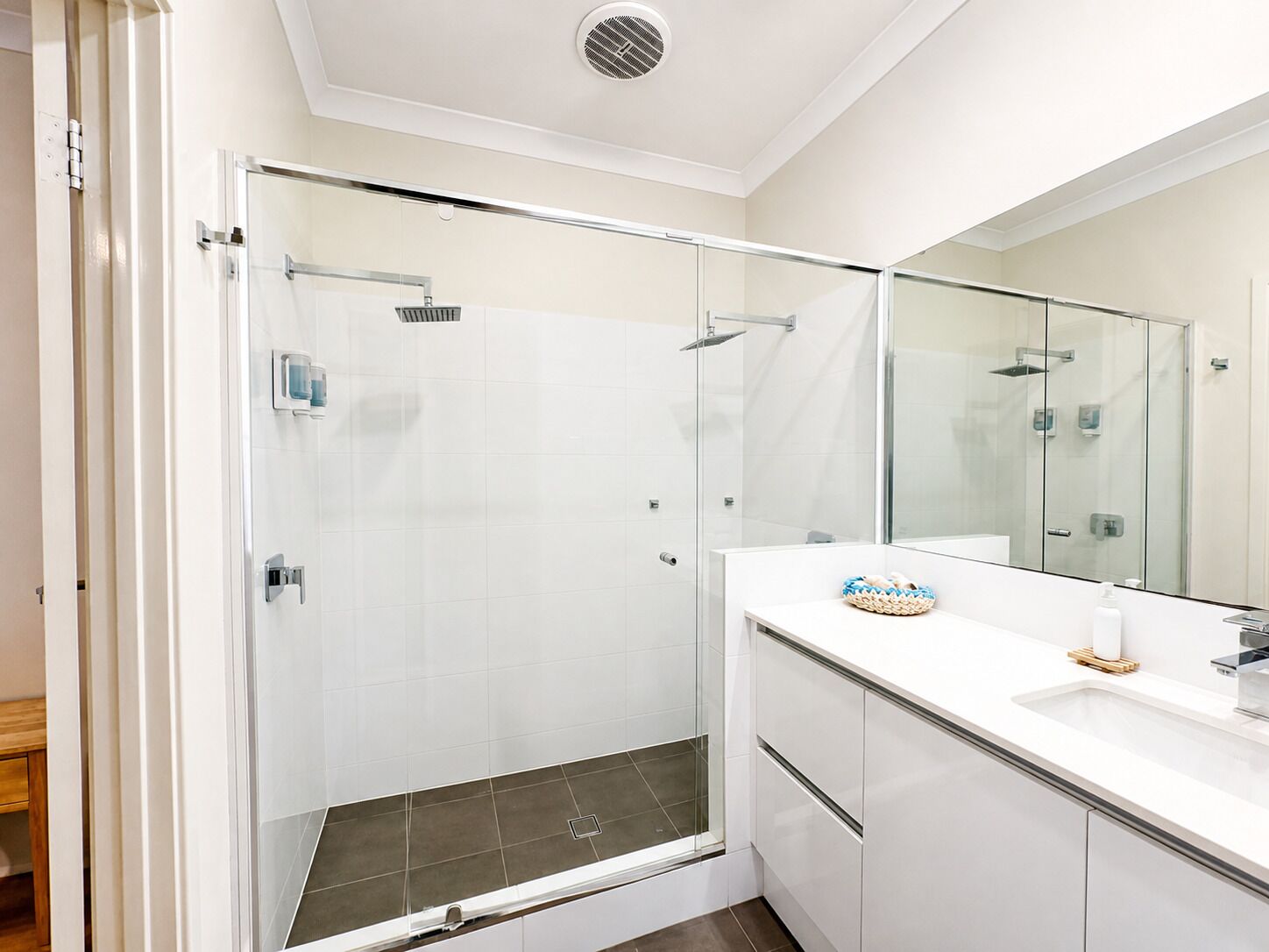 A modern bathroom with a glass-enclosed shower, a white vanity with a mirror, and a small sink.