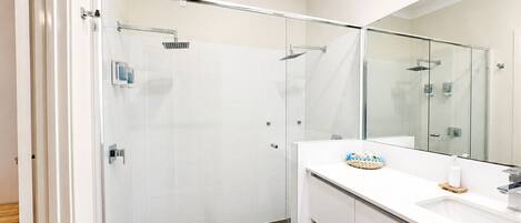 A modern bathroom with a glass-enclosed shower, a white vanity with a mirror, and a small sink.