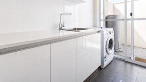 Une cuisine moderne avec des meubles blancs, un évier en acier inoxydable et un lave-linge à chargement frontal.