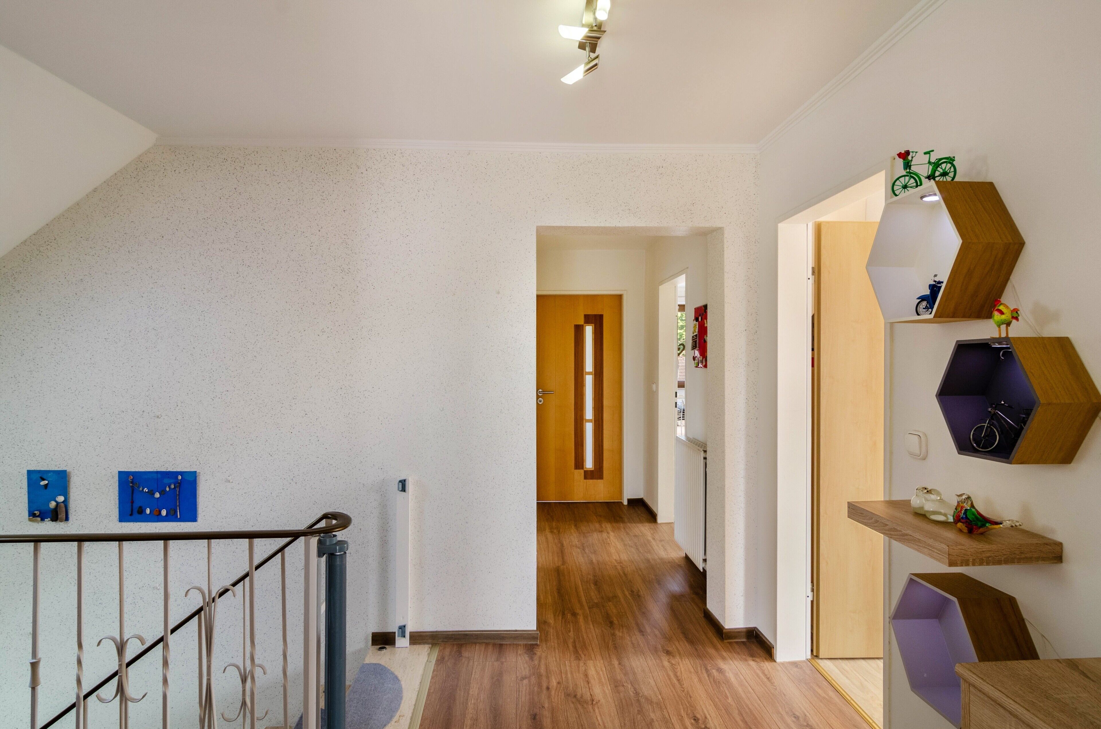 A hallway with wooden flooring, a staircase with a metal railing, and a wall with decorative shelves.