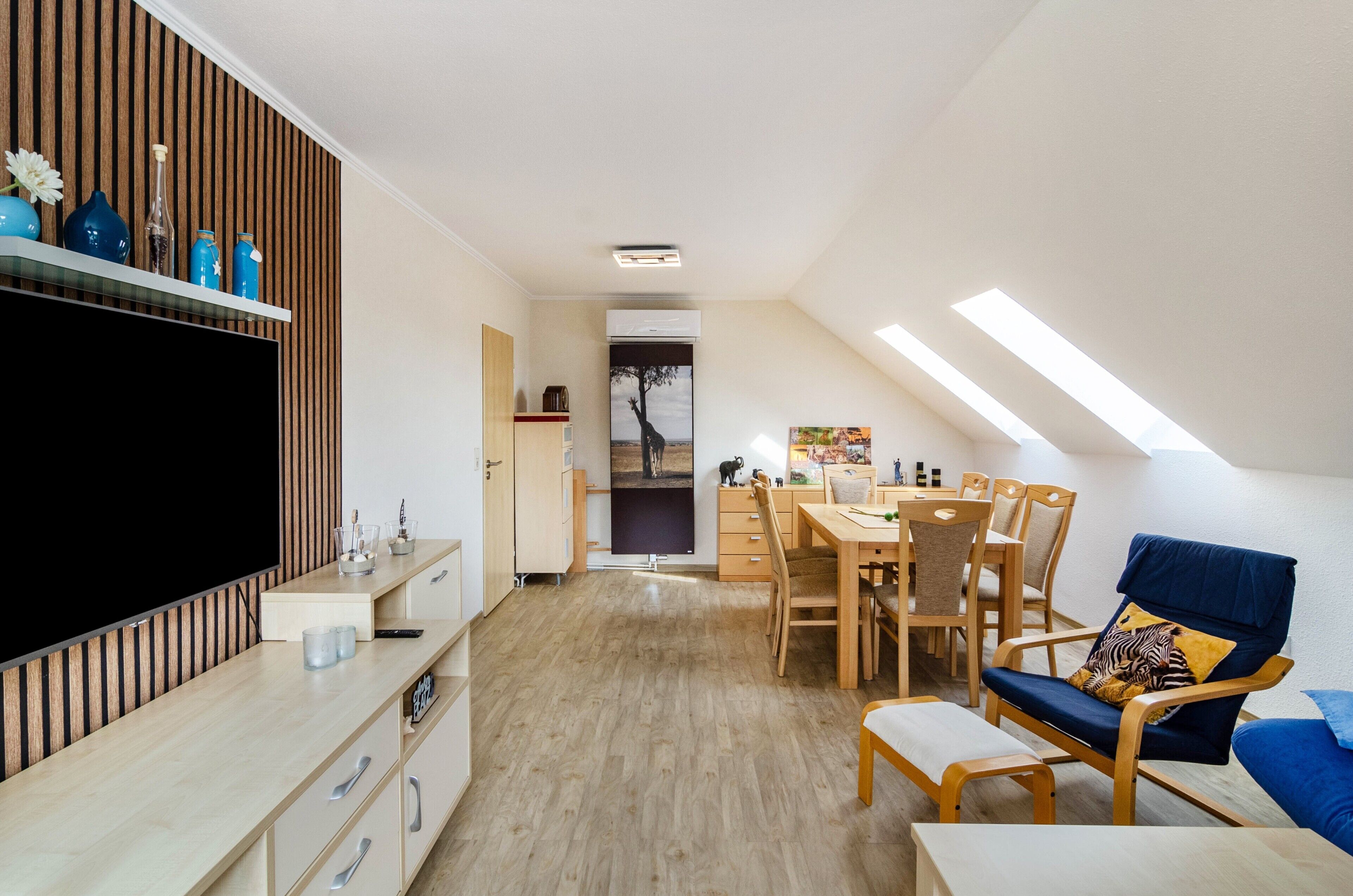A modern living space with a TV, wooden panel wall, dining area, and a blue chair.