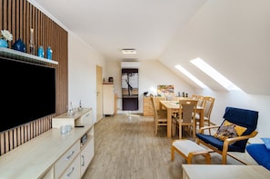 Un espacio de estar moderno con televisor, panel de pared de madera, zona de comedor y una silla azul.