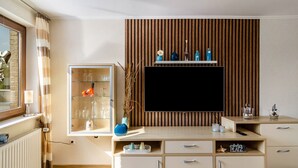Un salón moderno con televisor, pared de paneles de madera y vitrina con botellas.