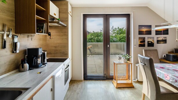 Una cocina moderna con horno empotrado, cafetera y lavabo. Hay una puerta corrediza de vidrio que da a un balcón con vistas a zonas verdes.