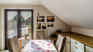 Una habitación pequeña y luminosa con una mesa de comedor, sillas, una pequeña cocina y un ventanal corredizo que da a un espacio exterior.