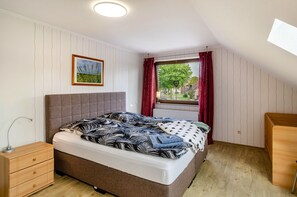 Un dormitorio con cama, mesita de noche y ventana con cortinas.