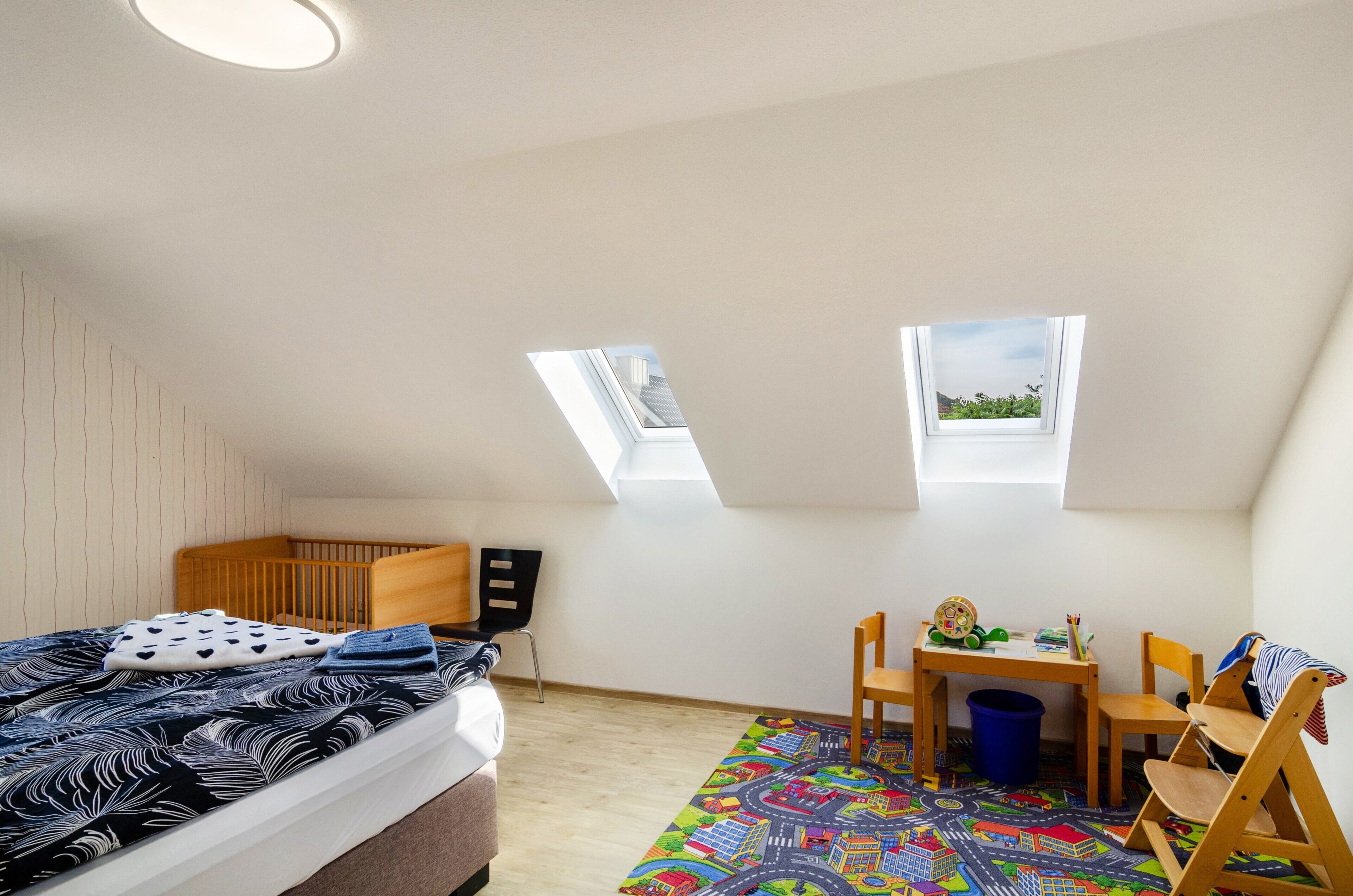 A room with a bed, a desk, two chairs, a window, and a skylight.