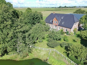 A large house with a sloped roof, surrounded by trees and a small pond.
