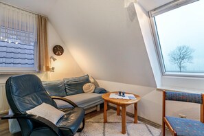 Tunnelmallinen huone, jossa on sohva, nojatuoli, pieni pöytä, kello ja ikkuna, josta on kaunis näkymä.