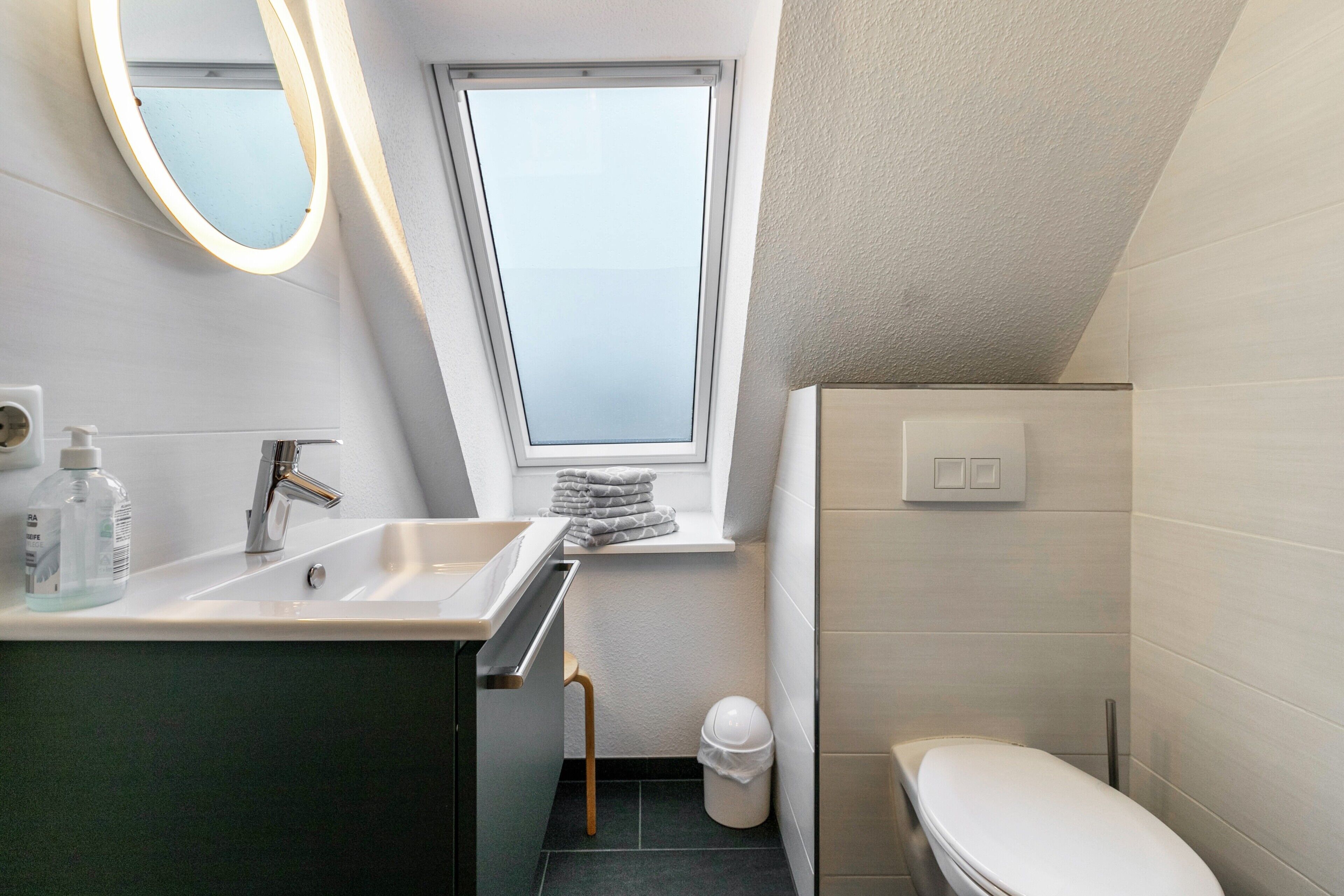 A small, modern bathroom with a window, a sink, a toilet, and a mirror.