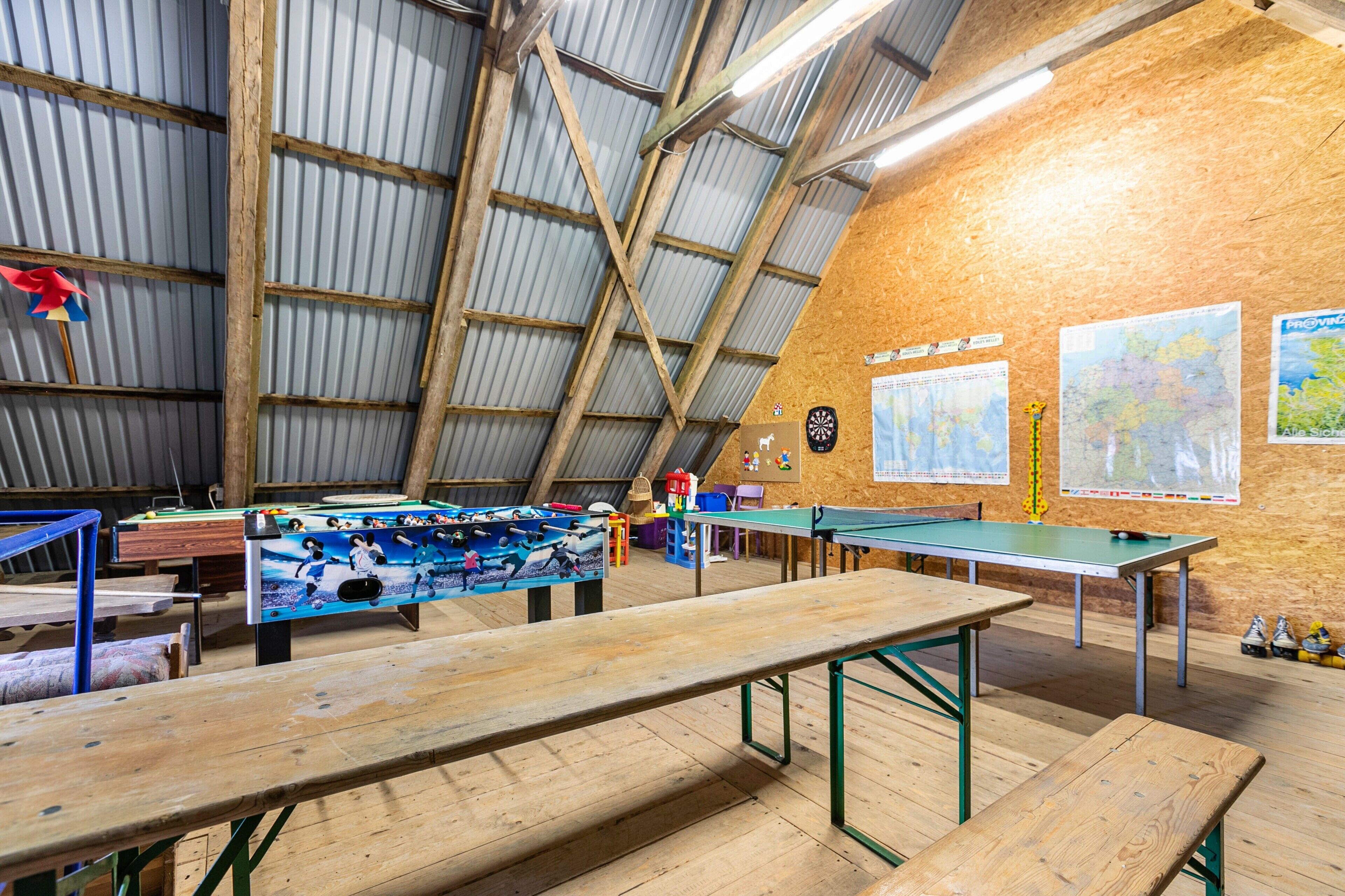 Un ambiente interno rustico con soffitto alto, travi in legno e un tavolo da ping pong.