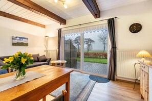Ein gemütliches Zimmer mit Holztisch, einer Couch, einer Lampe und Blick durch eine Glastür.
