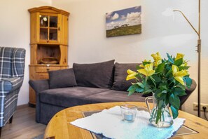 Un salon avec un canapé, un meuble en bois, un vase de fleurs et une lampe.