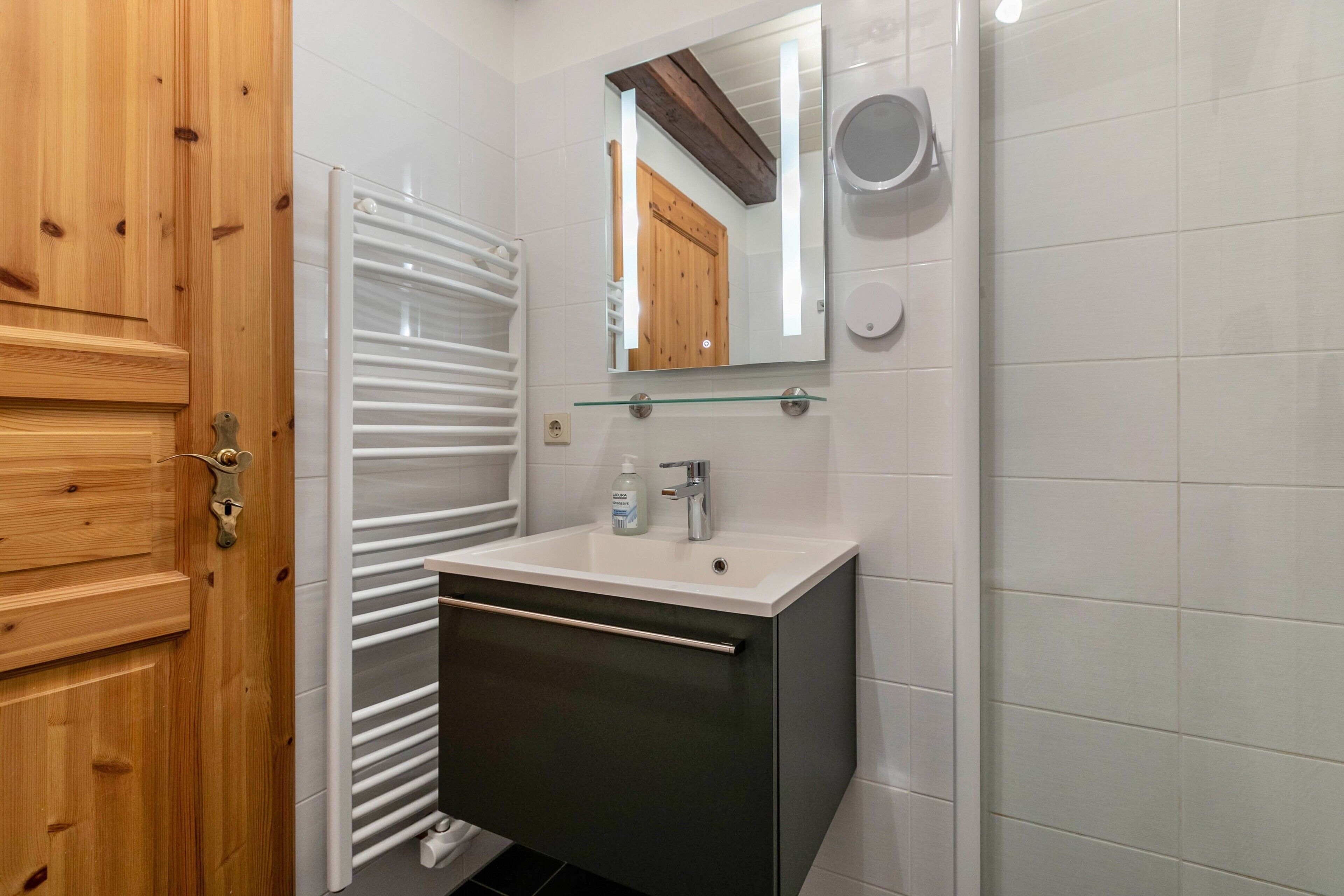 Un baño con puerta de madera, toallero blanco, espejo, lavabo y retrete.