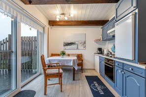 Une cuisine avec des meubles en bois, une table à manger avec des chaises et une vue à travers une porte vitrée.