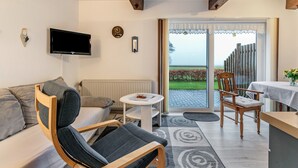 Een moderne woonkamer met een bank, een fauteuil, een bijzettafeltje, een televisie en een schuifpui die uitkomt op een buitenterras.
